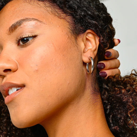 Close-up of a woman with styled hair and earrings against a neutral background