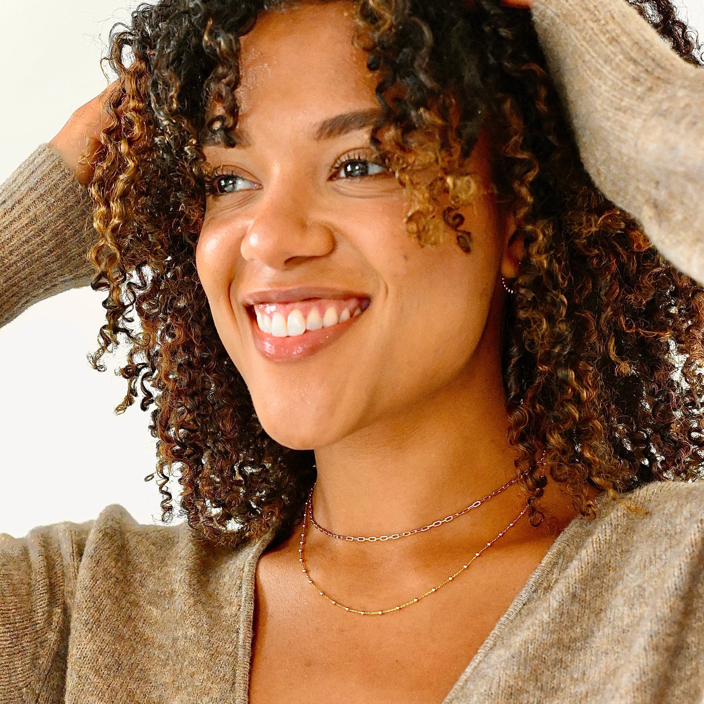 Woman with curly hair wearing a beige sweater against a white background